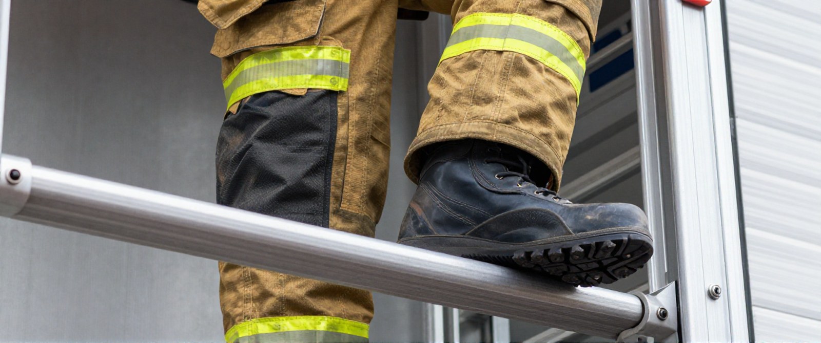 A firefighter standing on an aluminum ladder rung with the boot sole across the rung